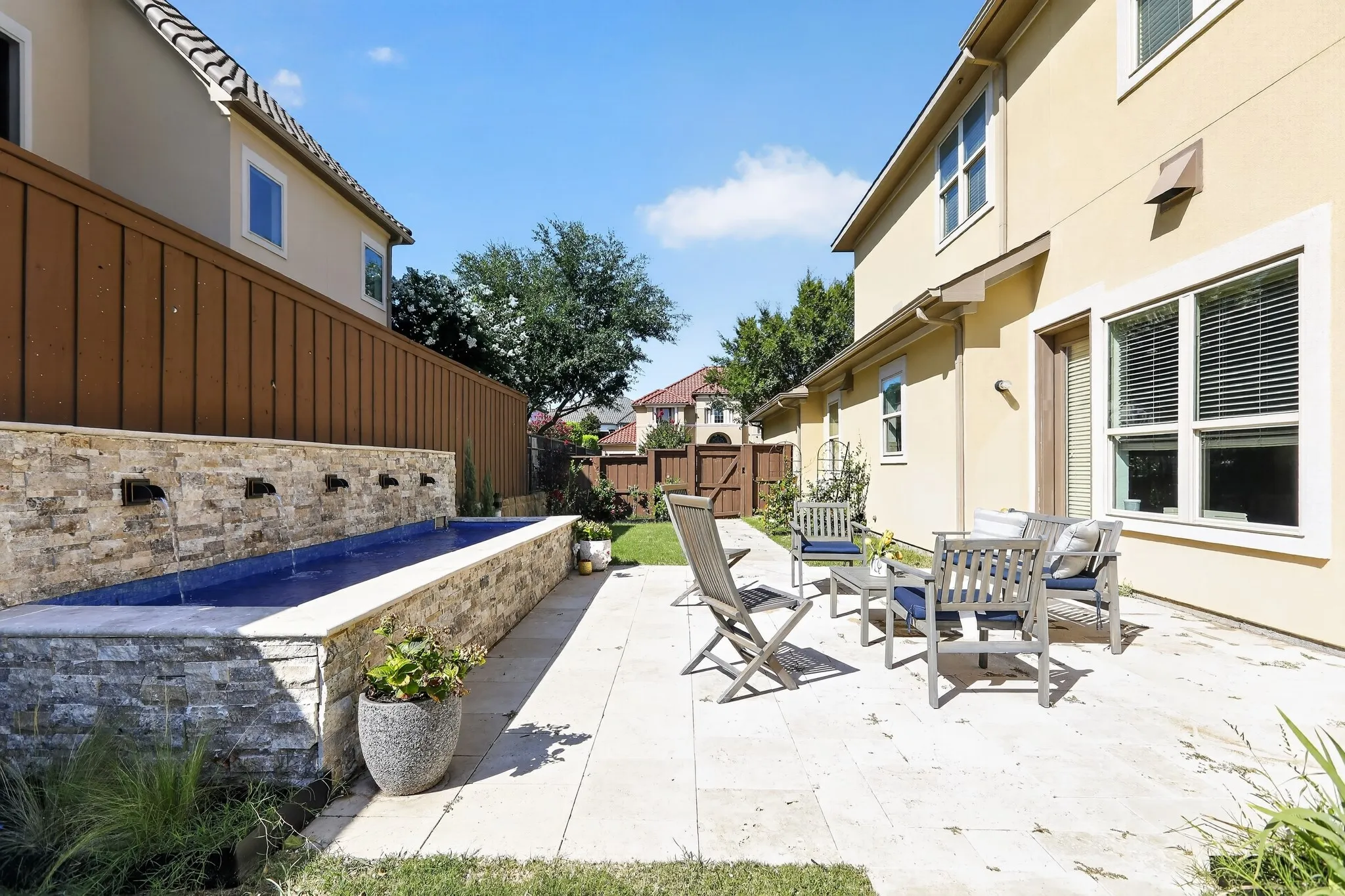 Exterior patio featuring a stone-clad water feature, stucco siding, a wood fence, and a grass lawn