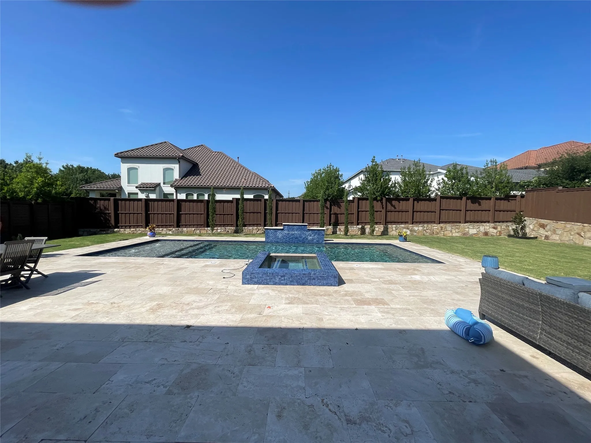 Expansive outdoor living area featuring a rectangular pool with a raised spa, surrounded by large format paver patio and green lawn