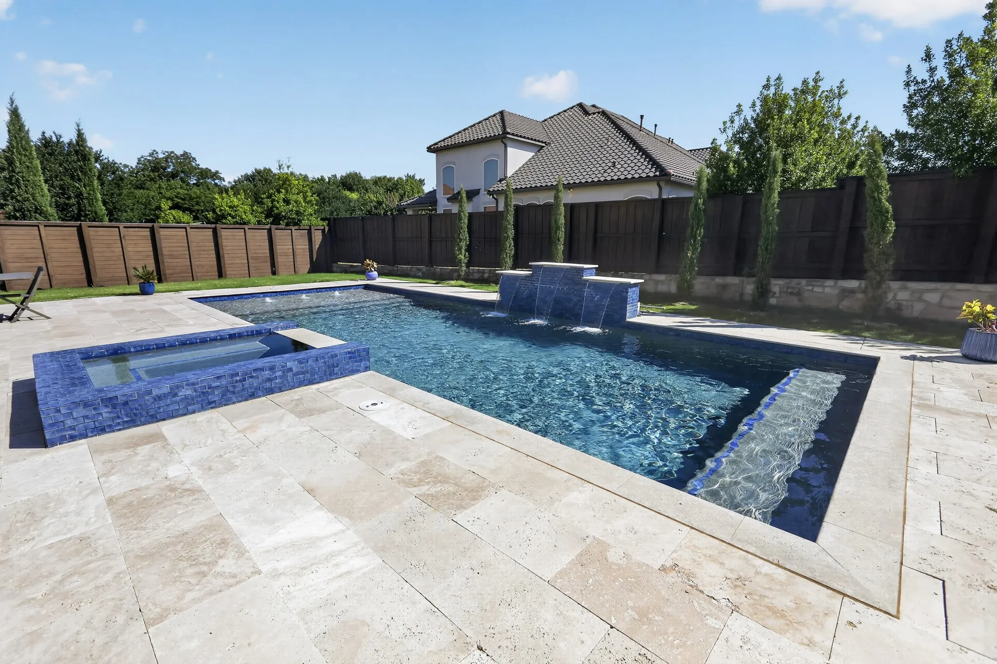 Contemporary swimming pool with integrated spa, featuring blue mosaic tile accents and a waterfall element
