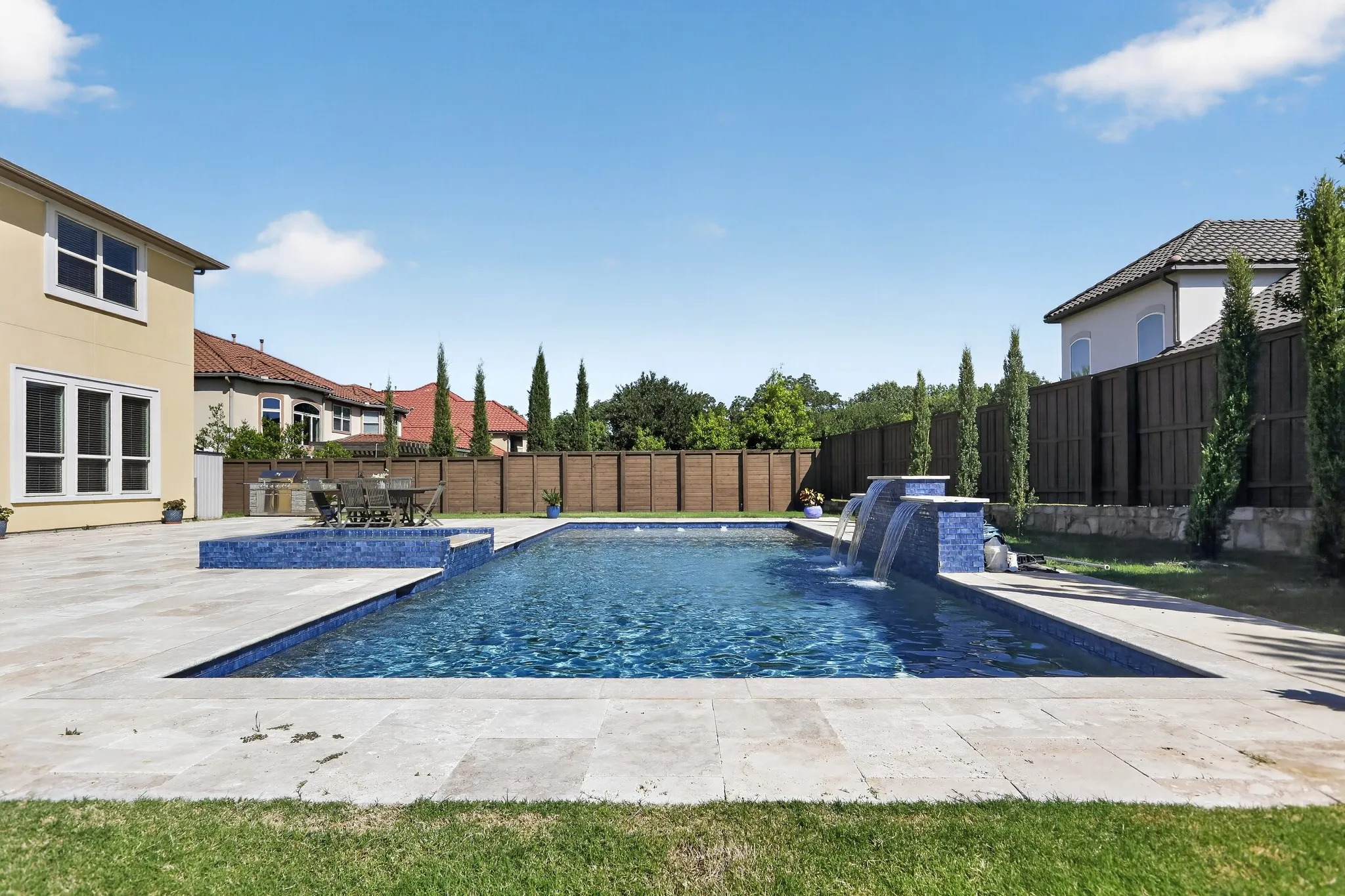 Expansive backyard featuring a rectangular swimming pool with integrated water features and a spa