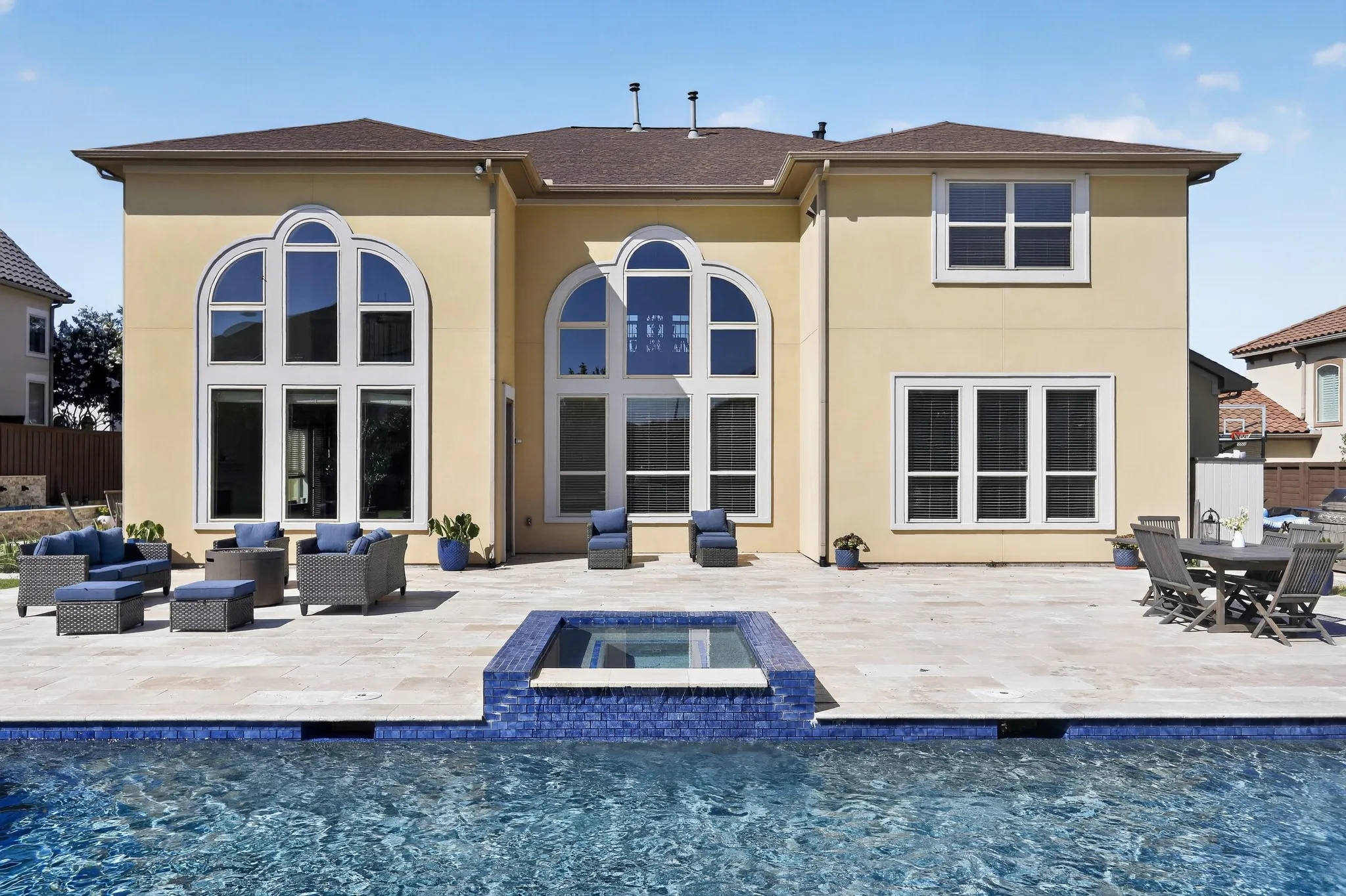 Expansive exterior patio featuring a built-in spa, a swimming pool with blue tile accents, and a light-colored paver surface