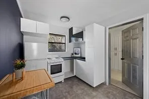 Compact kitchen featuring white cabinetry, dark countertops, and a white freestanding range