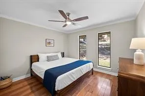 Bedroom featuring warm wood-finish flooring, light neutral wall tones, and crown molding