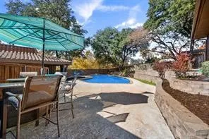 Outdoor concrete patio featuring an in-ground pool, stone retaining walls, and mature trees