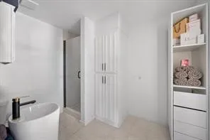 Modern bathroom featuring a contemporary pedestal sink with a matte black and gold-tone faucet, a glass-enclosed shower, and built-in vertical storage cabinetry