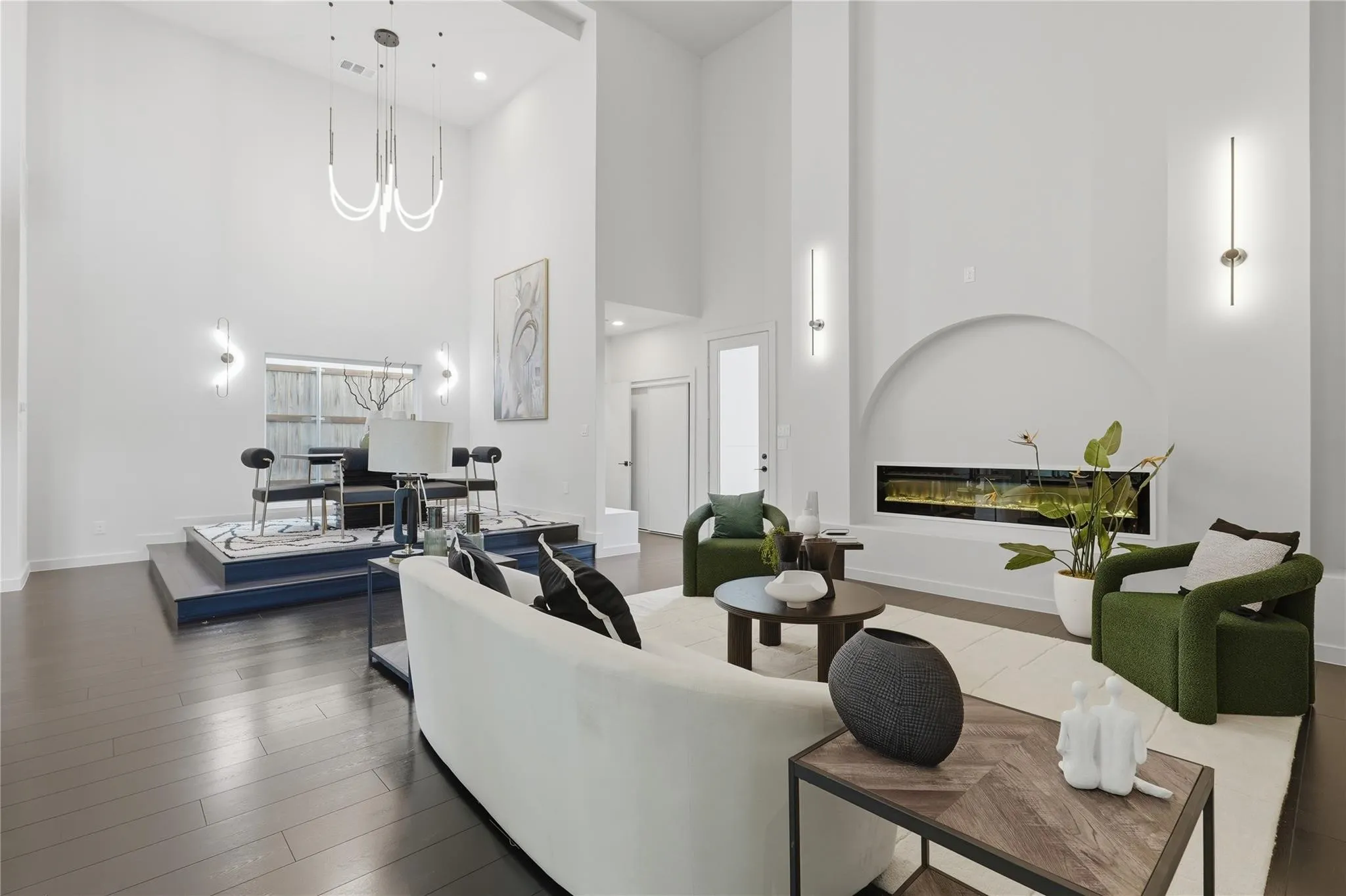 Open-concept living space with dark wood-finish flooring, soaring ceilings, a recessed linear fireplace, and a raised platform area
