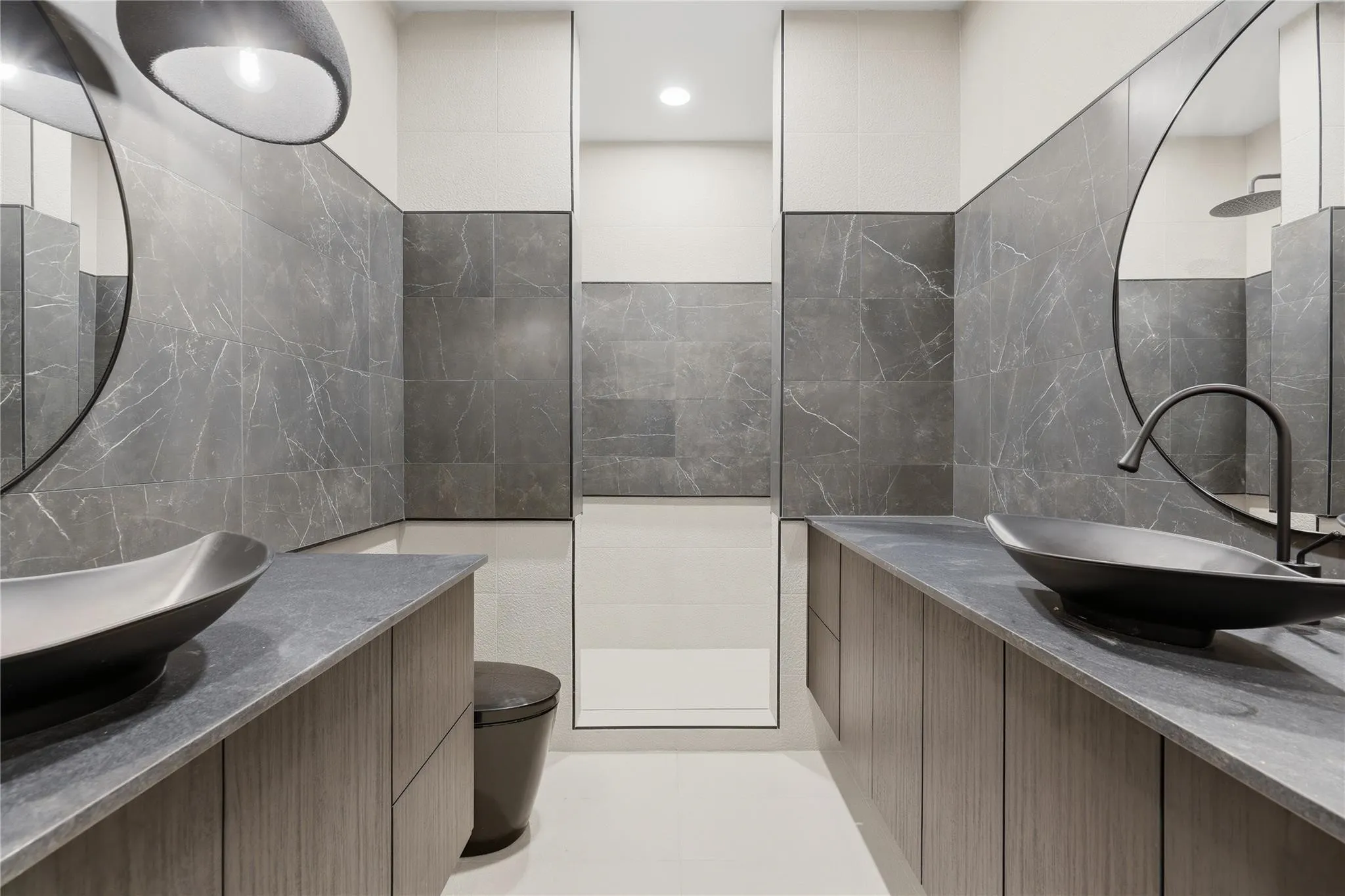 Dual floating vanities featuring wood-finish cabinetry, dark stone countertops, and vessel sinks with matte black fixtures