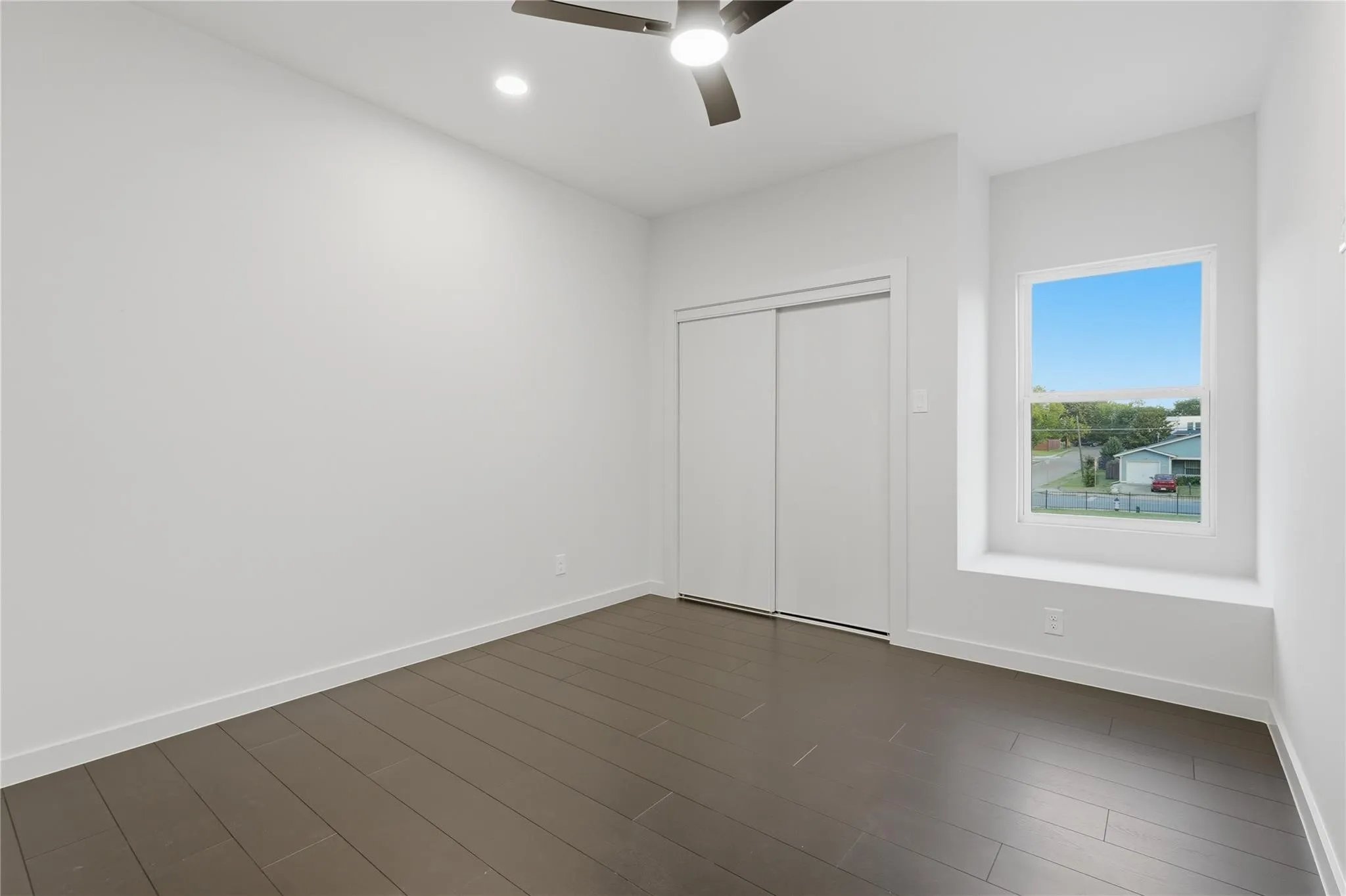 Spacious room featuring dark wood-finish flooring, a contemporary ceiling fan with integrated lighting, a recessed ceiling light, and a built-in window seat