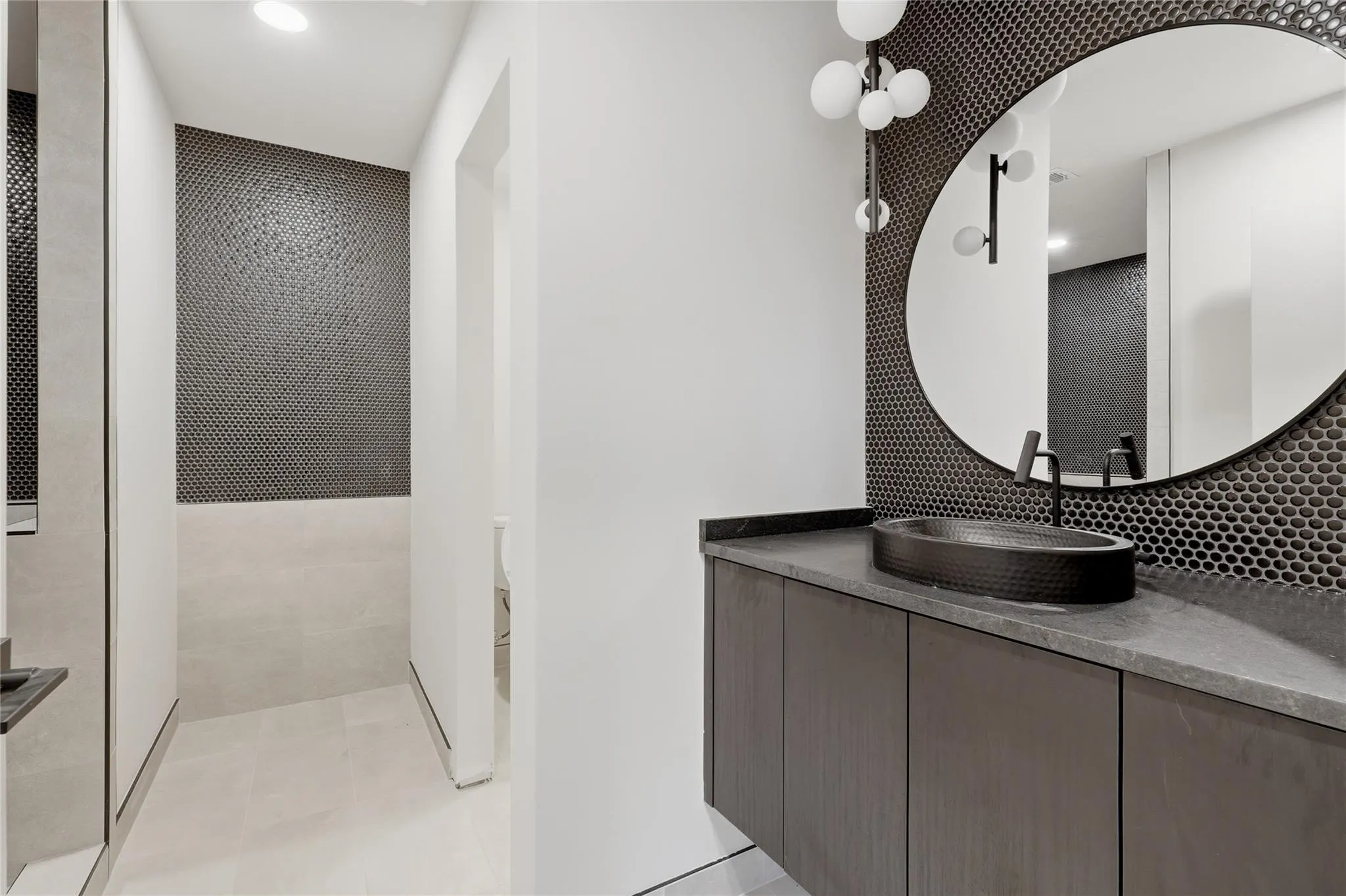 Modern bathroom vanity featuring a dark countertop, an oval vessel sink, and a black wall-mounted faucet