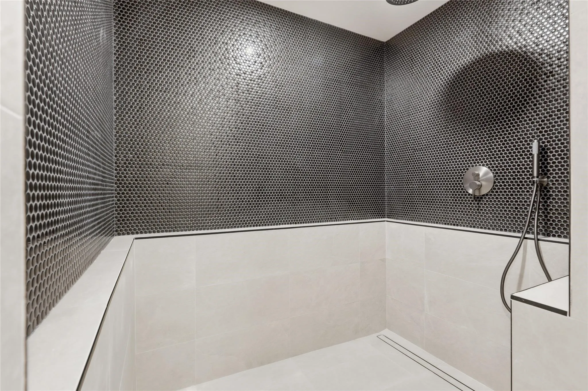 Shower enclosure featuring dark penny tile accent wall, light-toned large format ceramic wall tiles, recessed linear drain, brushed nickel shower controls, and a handheld showerhead