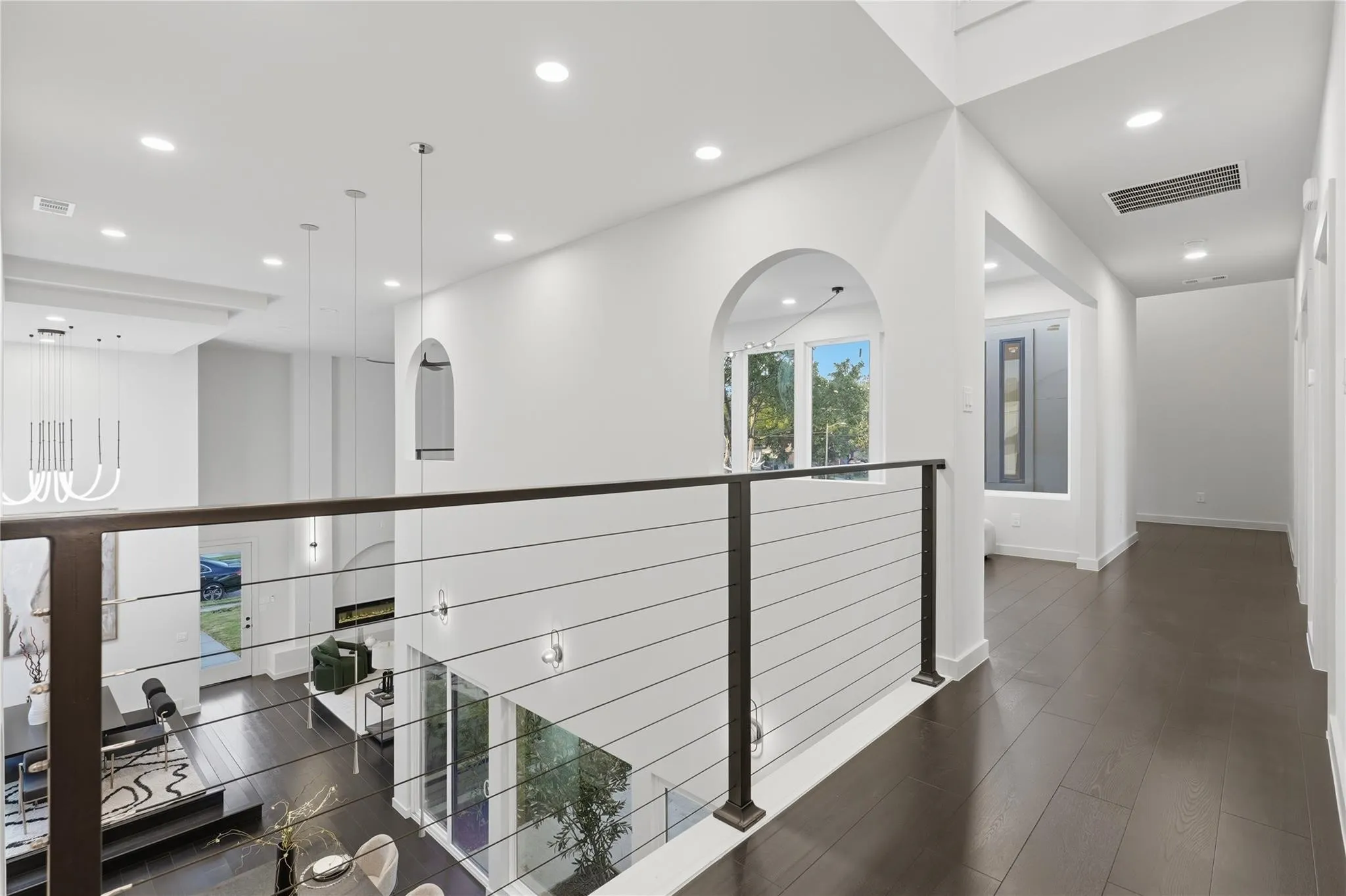 Upper-level hallway featuring dark wood-finish flooring, recessed lighting, and a contemporary cable railing system