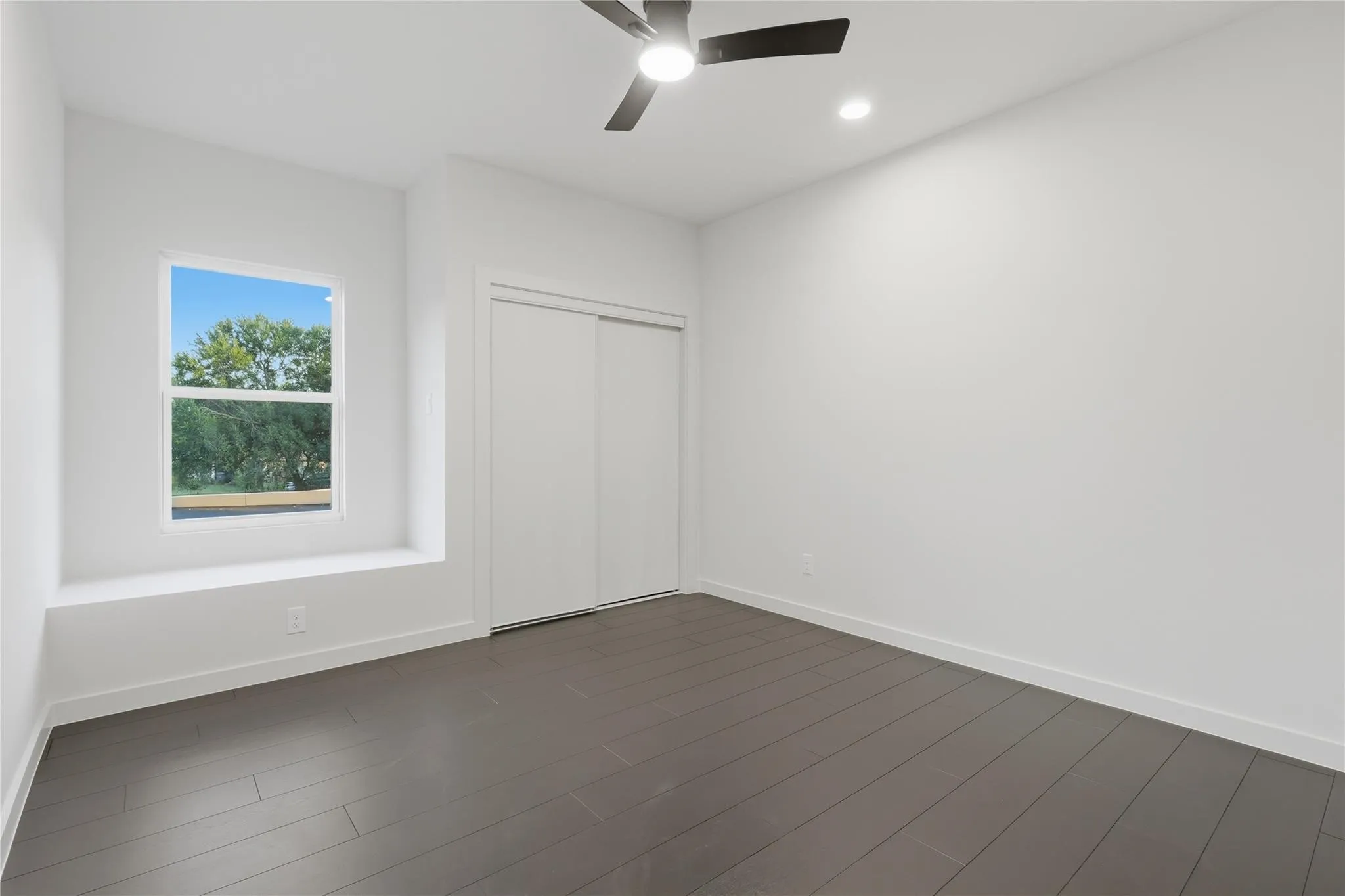 Bright room featuring dark wood-finish flooring, a contemporary ceiling fan, and recessed lighting