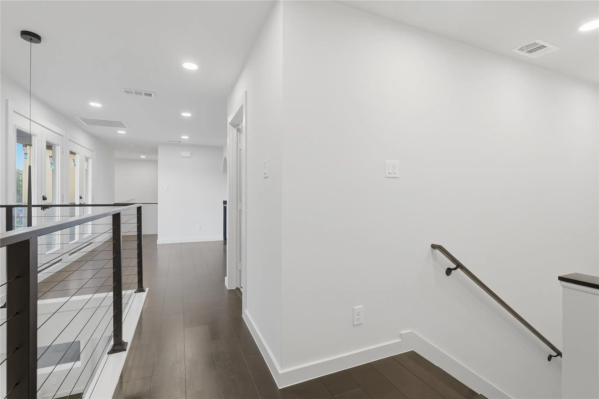 Upper-level hallway featuring dark wood-finish flooring, recessed lighting, white walls, and a contemporary cable railing system