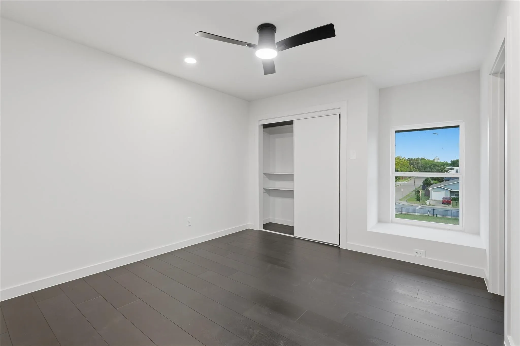 Spacious room featuring dark wood-finish flooring, a contemporary ceiling fan with integrated lighting, recessed lighting, and a white sliding door closet with built-in shelving
