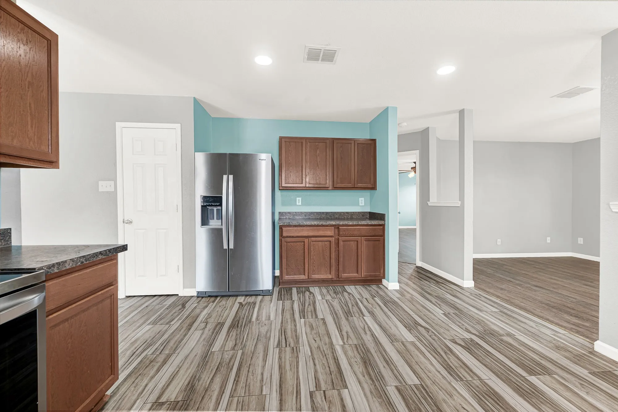 Kitchen featuring wood-finish flooring, recessed lighting, wood cabinetry, dark countertops, and a stainless steel refrigerator