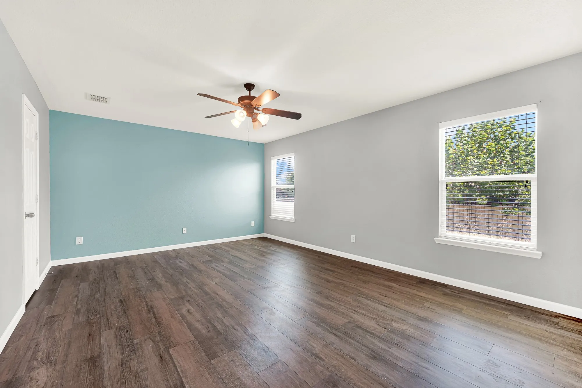Spacious room featuring wood-finish flooring, a ceiling fan with integrated lighting, and a prominent accent wall