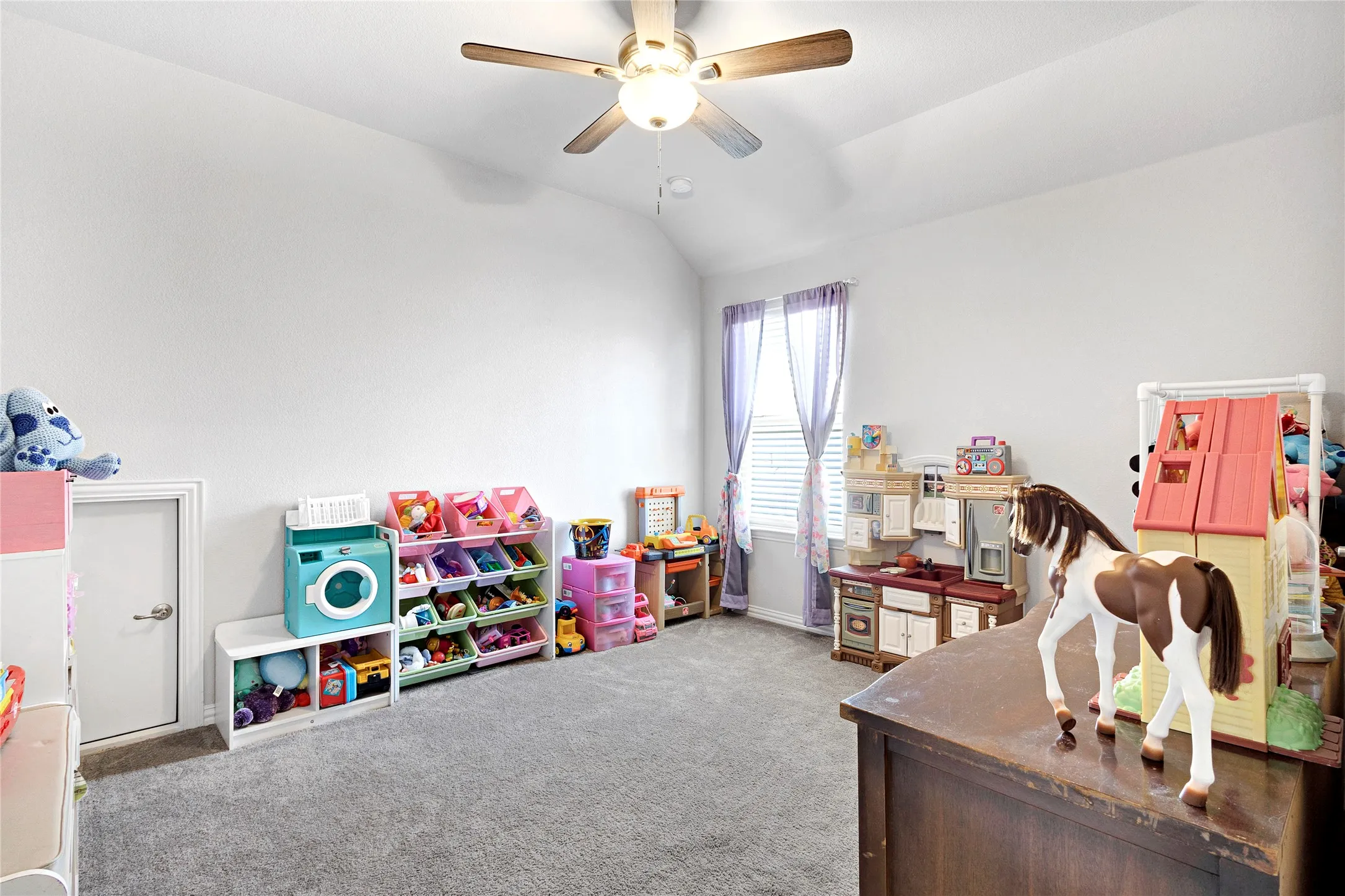 Room featuring a vaulted ceiling with a ceiling fan, a window with blinds, and light gray carpeting