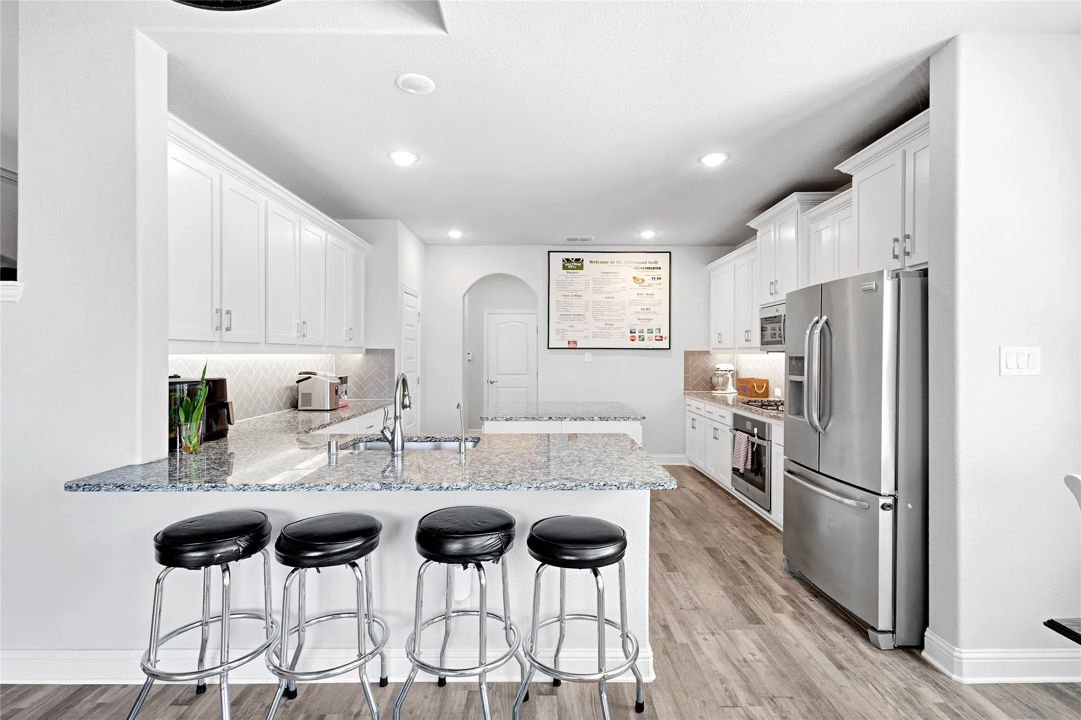 Kitchen featuring an expansive island with granite countertop, white cabinetry, stainless steel appliances, and wood-finish​​‌​​​​‌​​‌‌​‌‌​​​‌‌​‌​‌​‌​​​‌​​ flooring