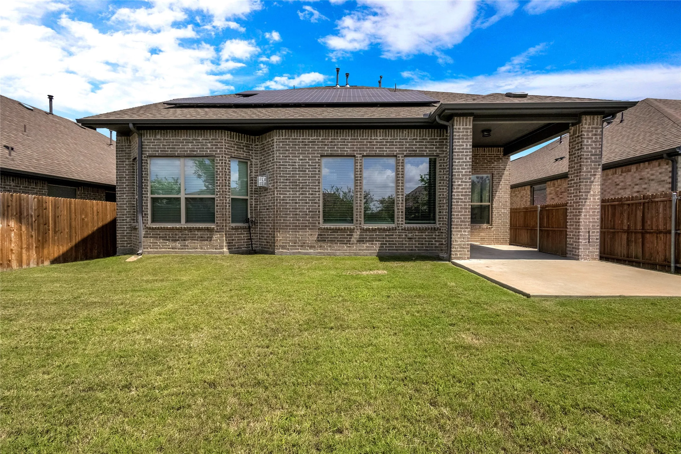 Expansive rear exterior featuring a brick facade, covered patio, multiple windows, and a manicured lawn