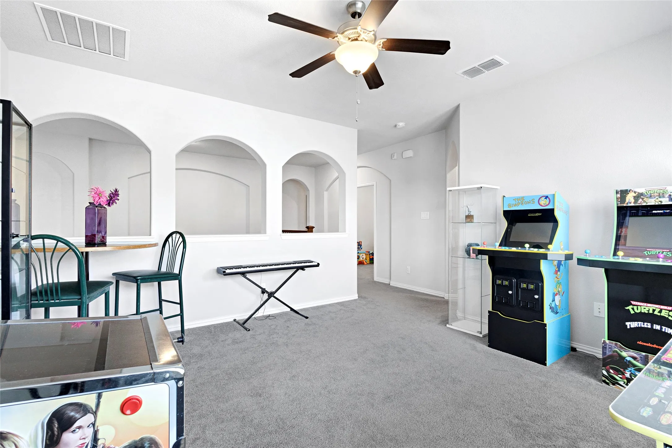 Carpeted interior space featuring a ceiling fan with integrated lighting, arched wall cutouts, and neutral paint