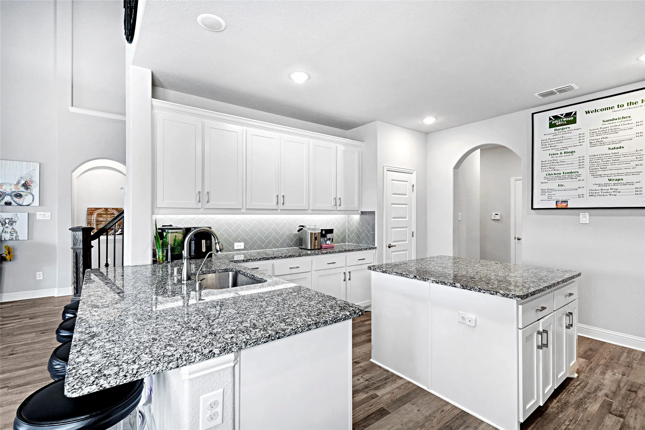 Modern kitchen featuring white cabinetry, granite countertops, an undermount sink, a herringbone tile backsplash, and wood-finish flooring