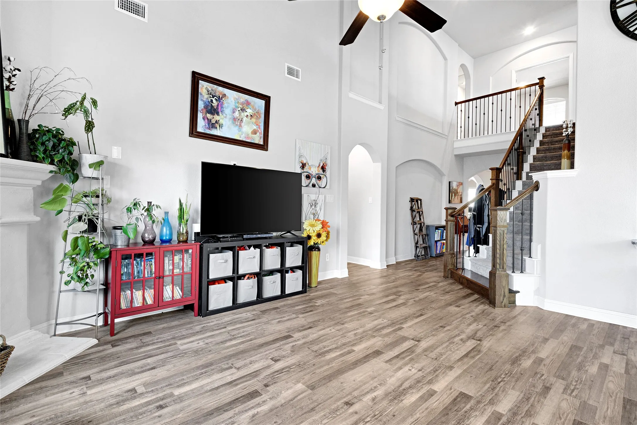 Spacious living area featuring high ceilings, wood-finish flooring, a decorative fireplace mantel, and an elegant staircase with wood and wrought iron railings