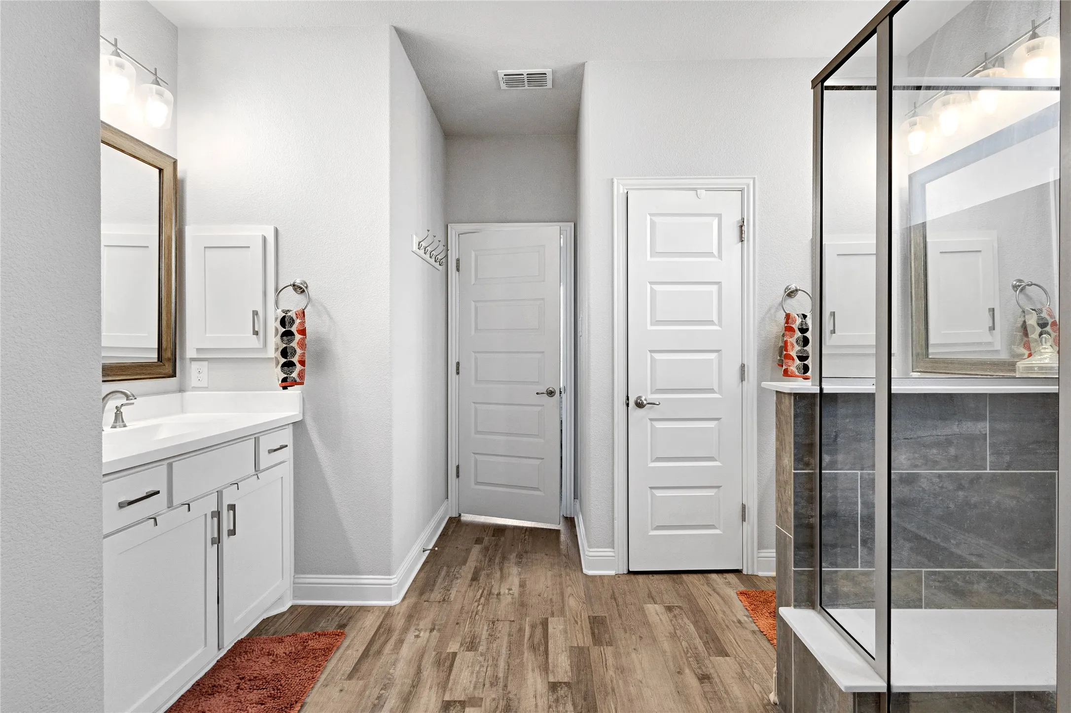 Bathroom featuring a glass-enclosed shower, single vanity with white cabinetry, wood-finish flooring, and two paneled doors