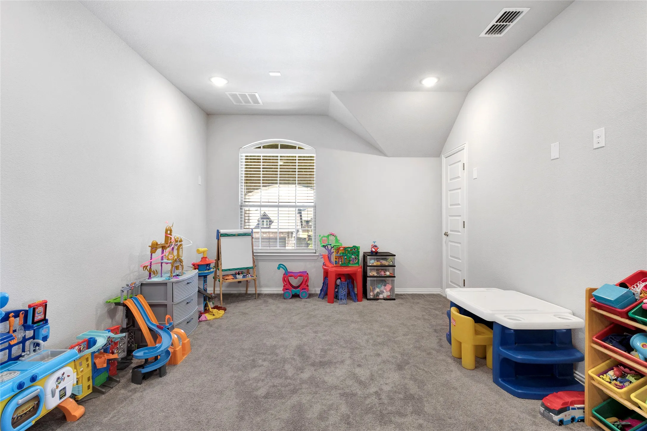 Spacious room featuring gray carpeting, white walls, and an arched window with blinds