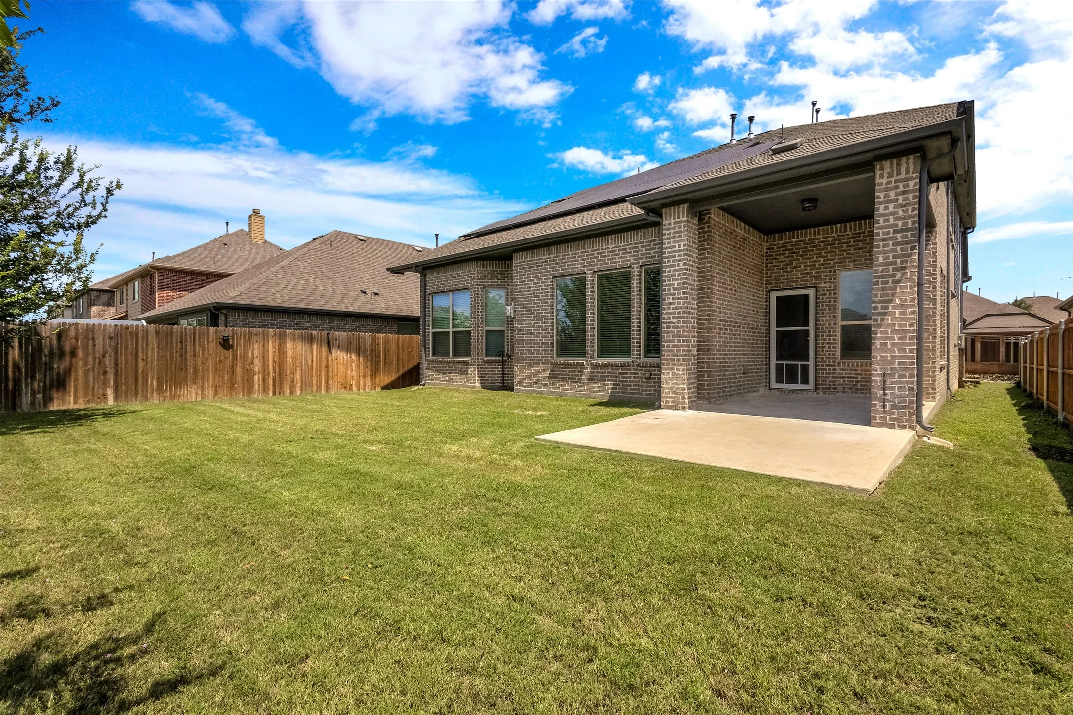 Expansive backyard featuring a manicured lawn, a covered patio with concrete flooring, a full brick exterior, and a wood privacy fence
