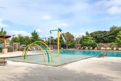 Resort-style aquatic amenity featuring a swimming pool, integrated splash pad with colorful water features, and an expansive concrete deck