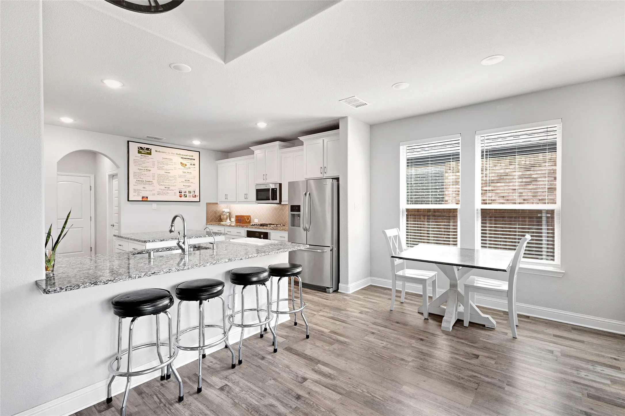 Open-concept kitchen featuring an expansive granite island, white cabinetry, stainless steel appliances, and recessed lighting