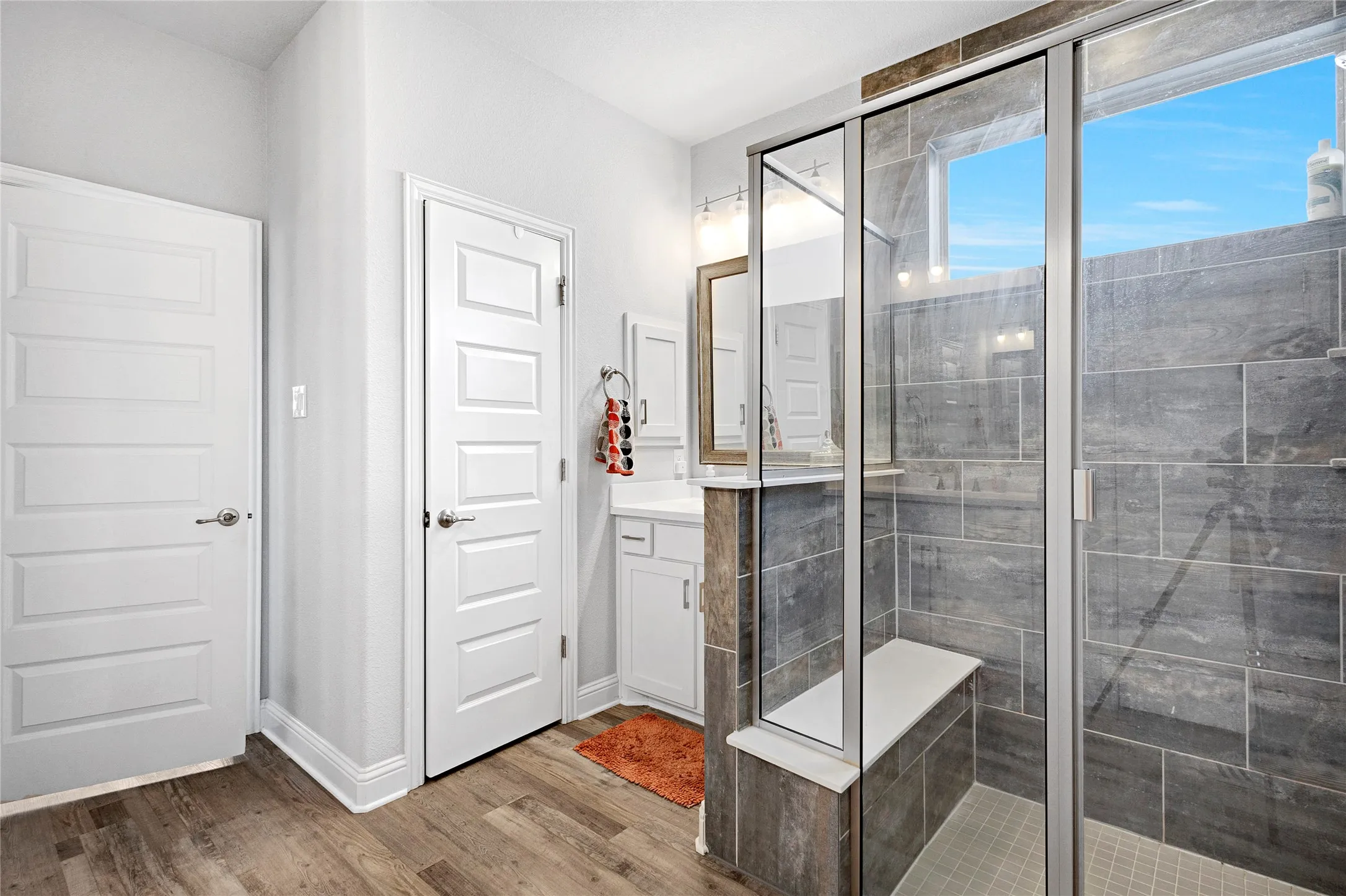 Expansive walk-in shower featuring gray tile surround, glass enclosure, and an integrated bench seat