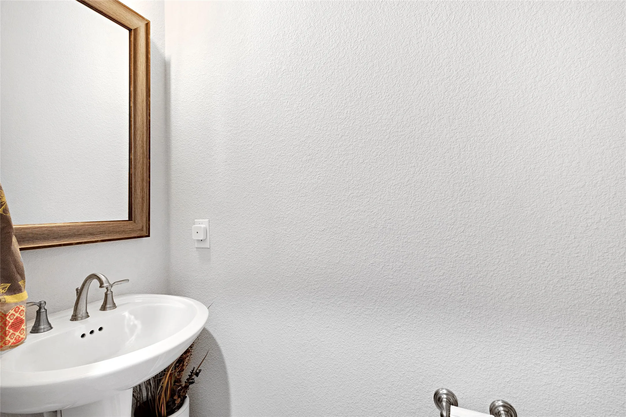 Pedestal sink with brushed nickel faucet, framed mirror, and textured white wall finish