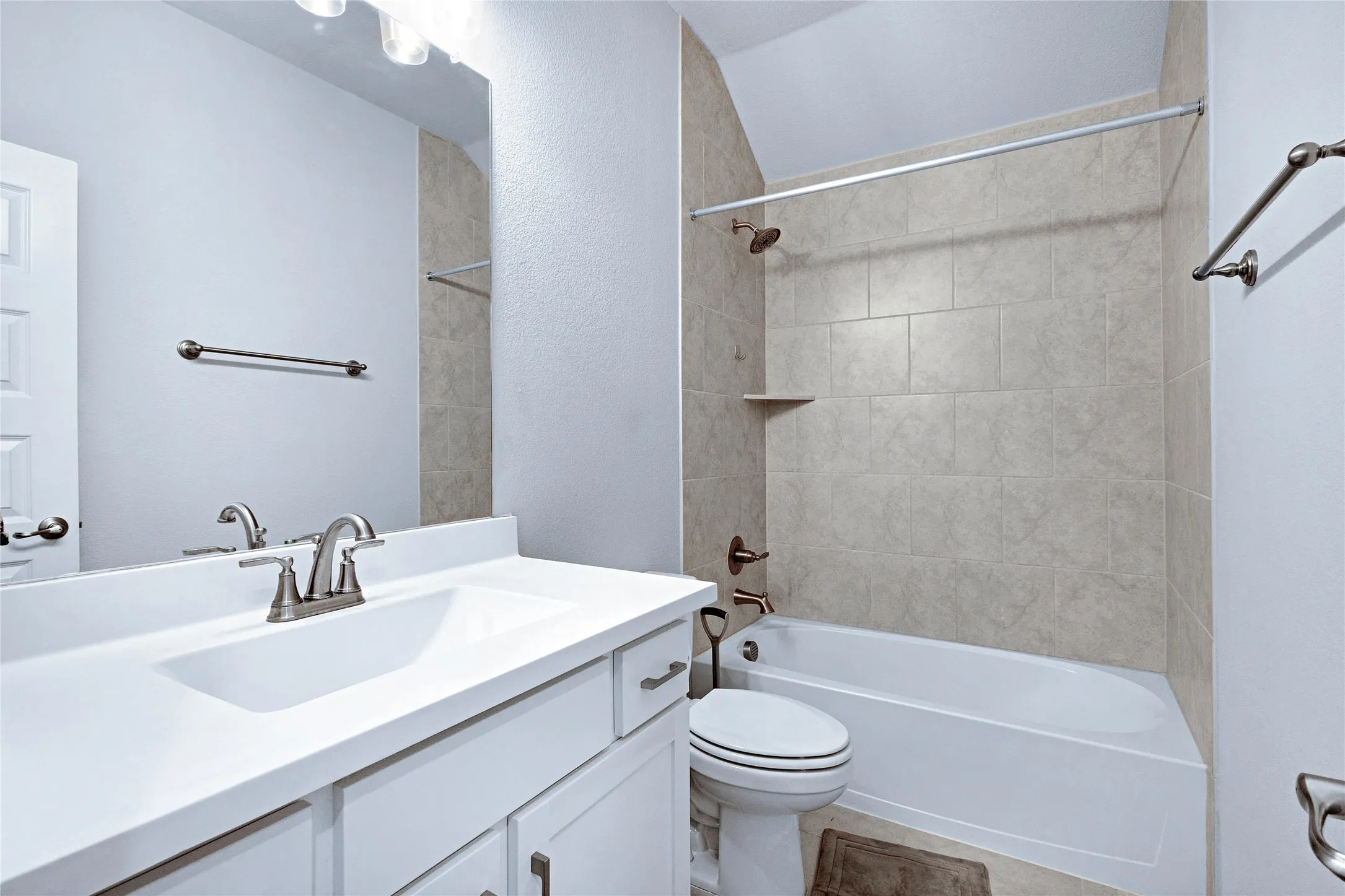 Bathroom featuring a white vanity with integrated sink, brushed nickel faucet, large mirror, and overhead vanity lighting