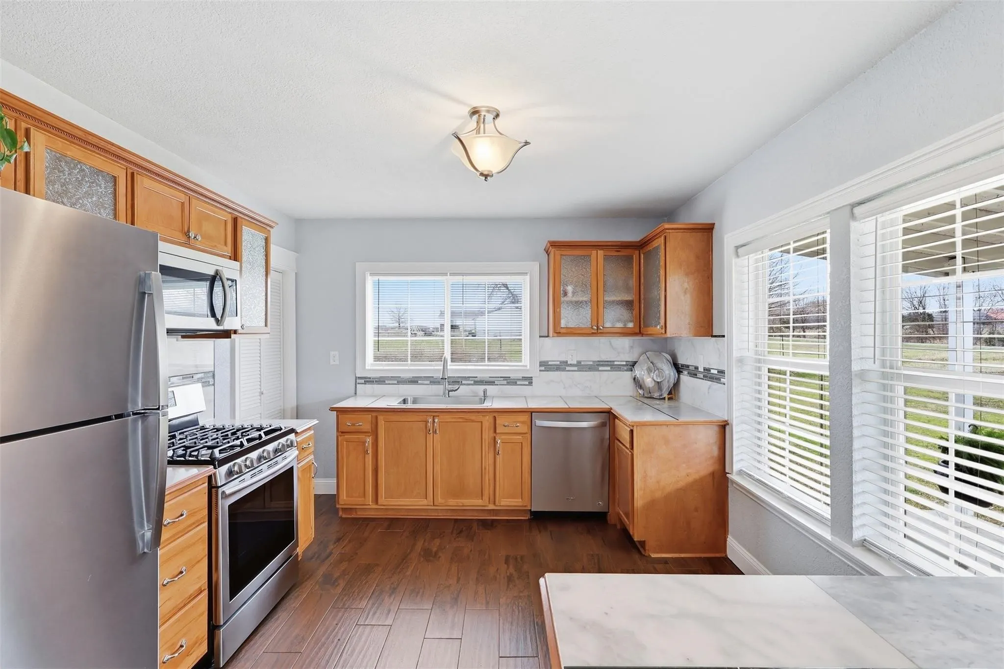 Kitchen featuring natural wood cabinetry, stainless steel appliances, a mosaic tile backsplash, wood-finish flooring, and multiple windows