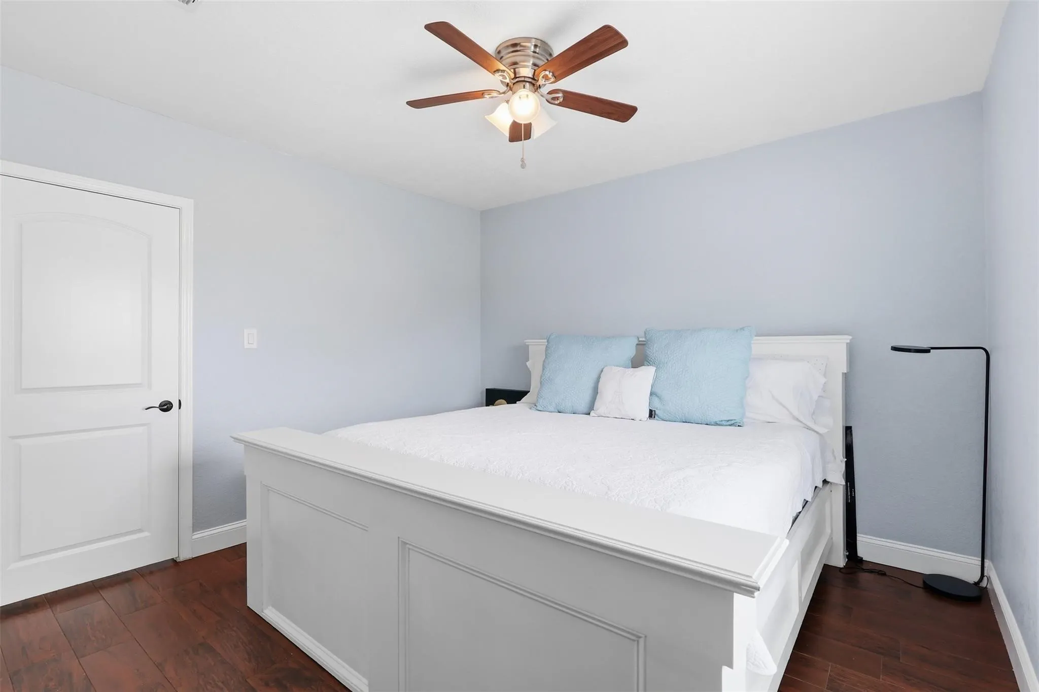 Room with wood-finish flooring, a ceiling fan with integrated lighting, and a paneled interior door with dark hardware