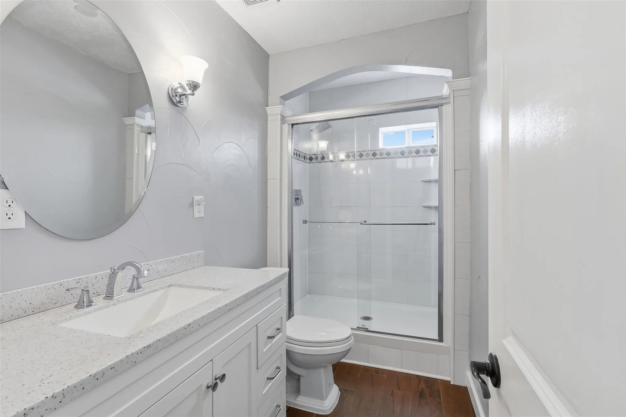 Bathroom featuring a white vanity with a speckled countertop, an undermount sink, and a large round mirror