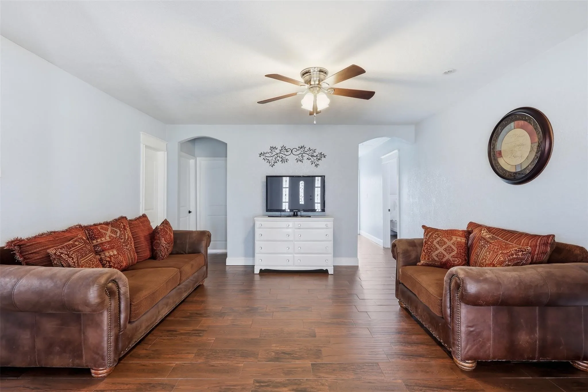 Spacious living area featuring wood-finish flooring, light-toned walls, and a ceiling fan with integrated lighting
