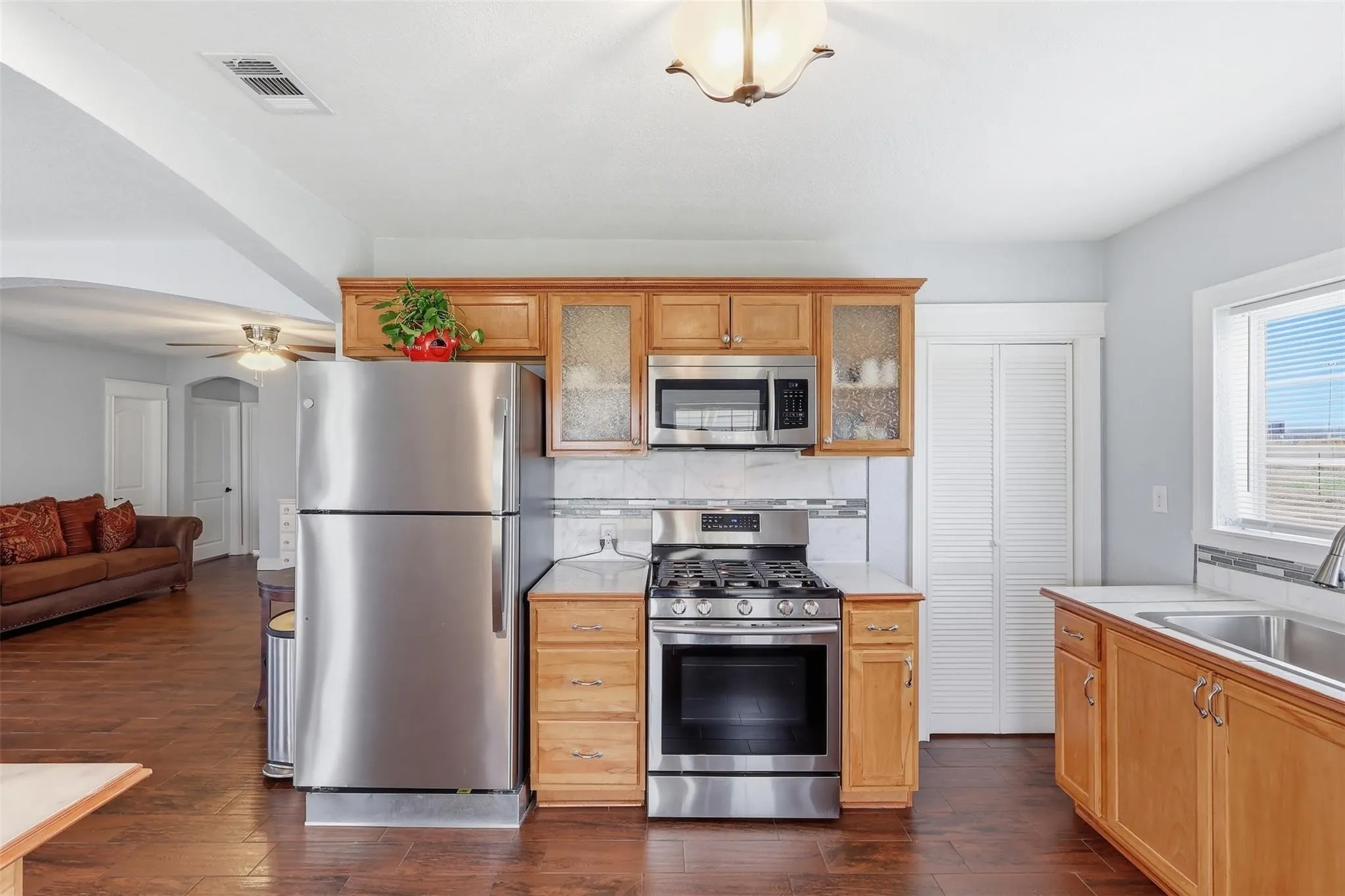 Kitchen featuring wood-finish flooring, light wood cabinetry, stainless steel appliances, and tile backsplash