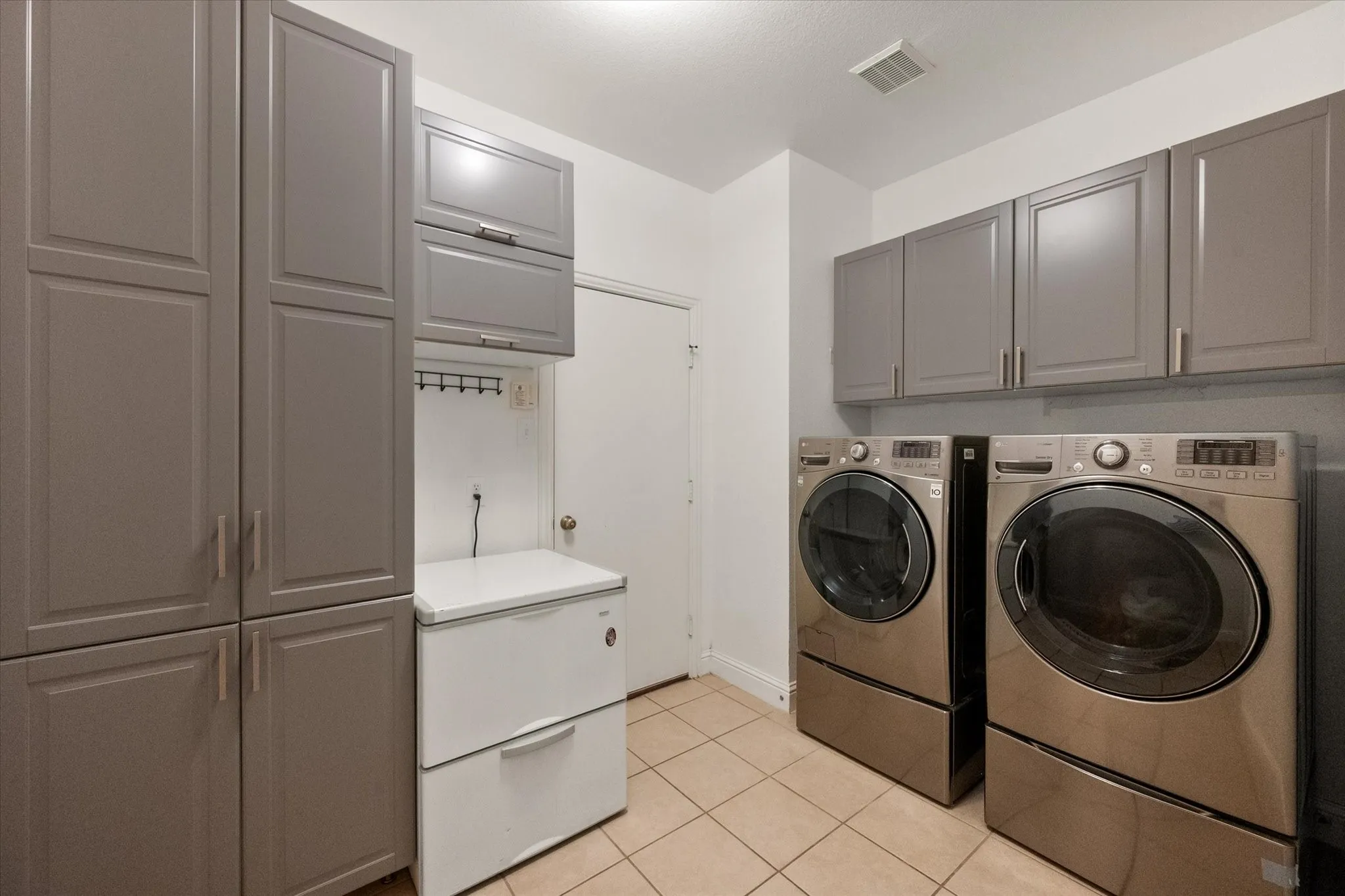 Laundry area with garage enterance, featuring extensive gray cabinetry providing ample storage, ceramic tile flooring, and a white ceiling with a flush-mount light fixture
