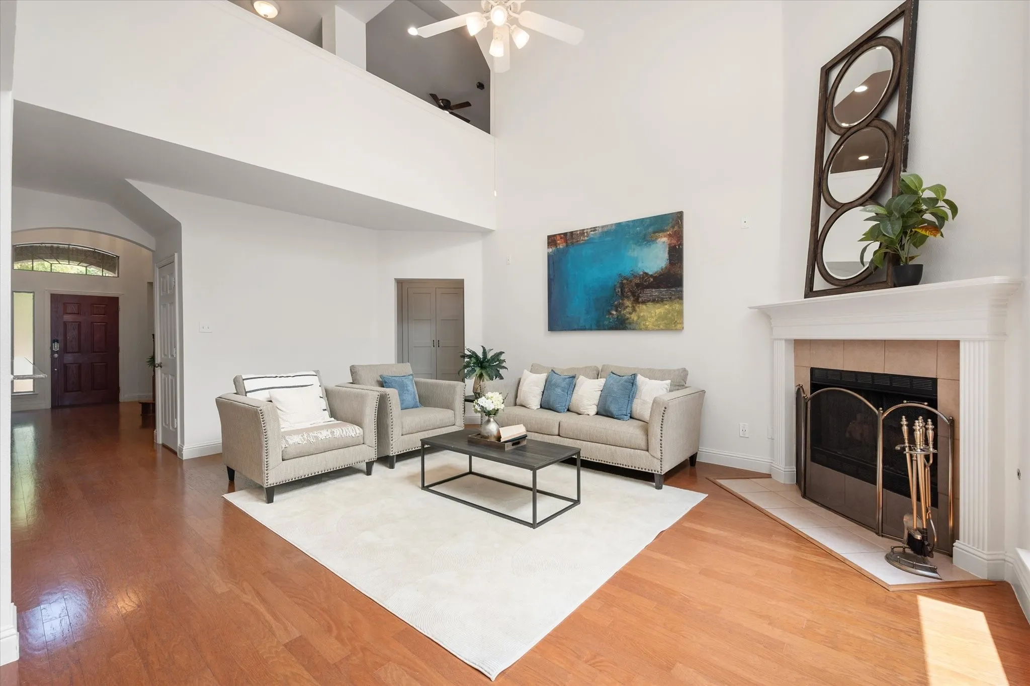 Spacious living area featuring high ceilings, wood-finish flooring, a fireplace with a white mantel, and an arched entryway