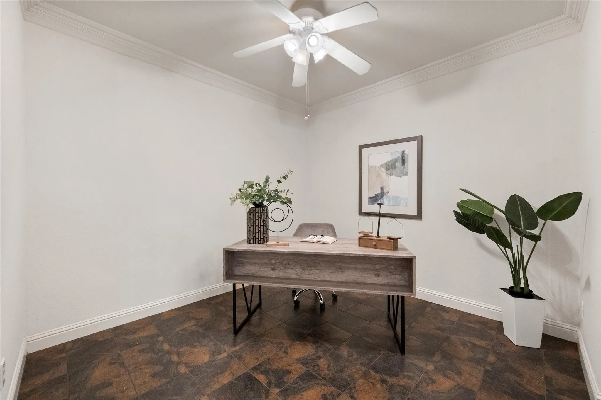 Interior room featuring neutral wall paint, dark-toned tile flooring, white crown molding, white baseboards, and a ceiling fan with integrated lighting