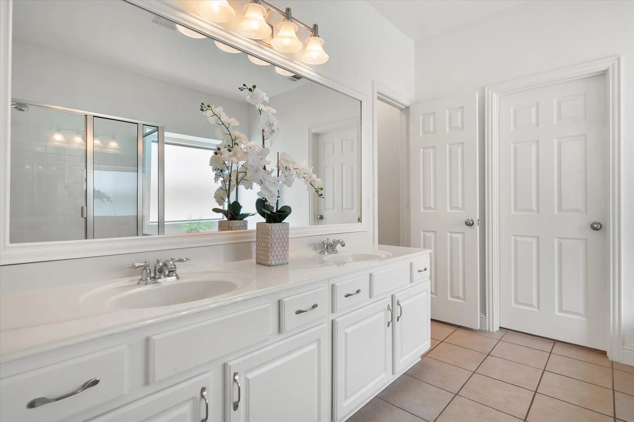 Dual vanity featuring white cabinetry, integrated sinks, chrome fixtures, and a large wall-mounted mirror