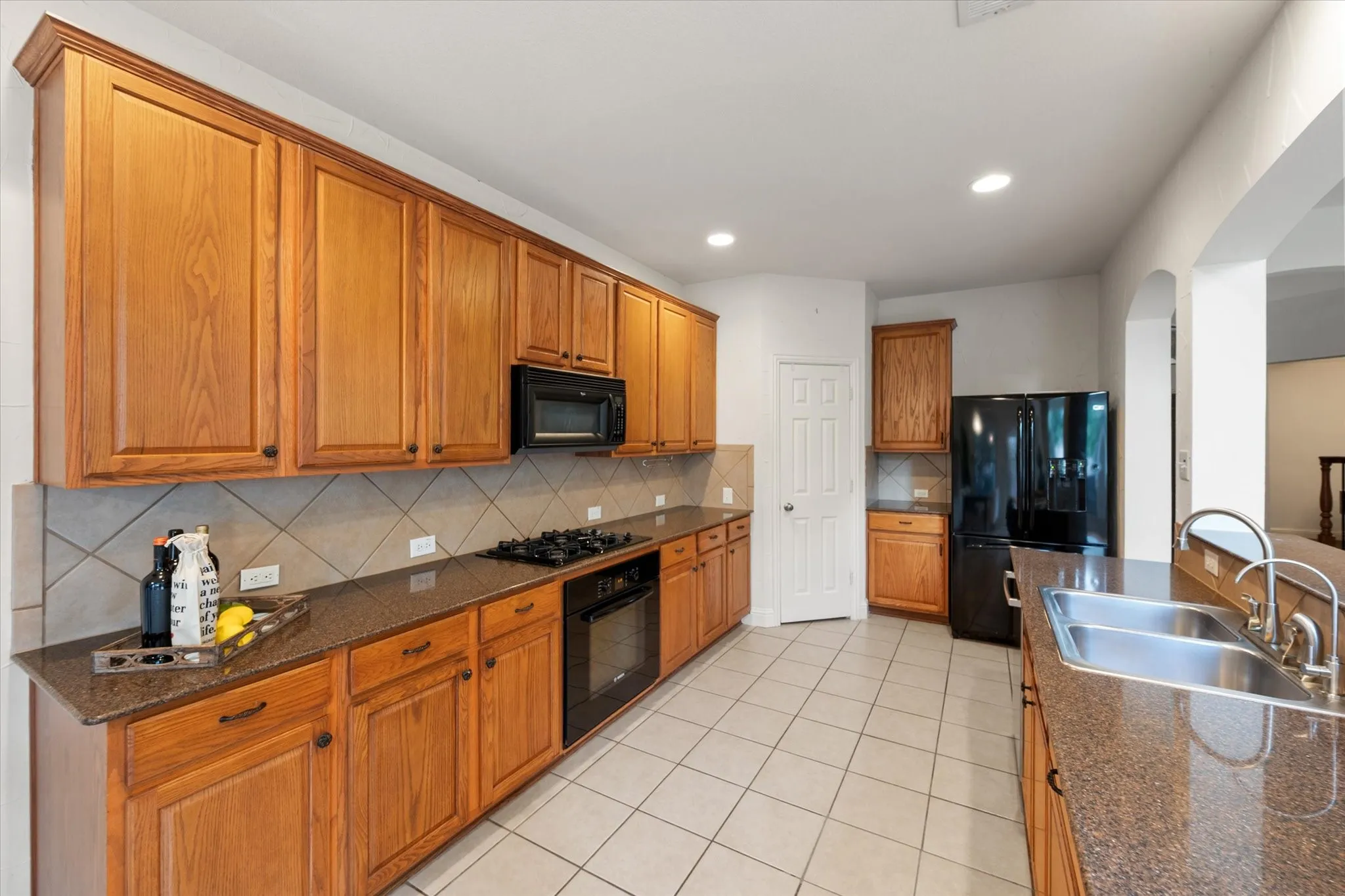 Kitchen featuring wood cabinetry, granite-style countertops, tile flooring, and integrated stainless steel double sink