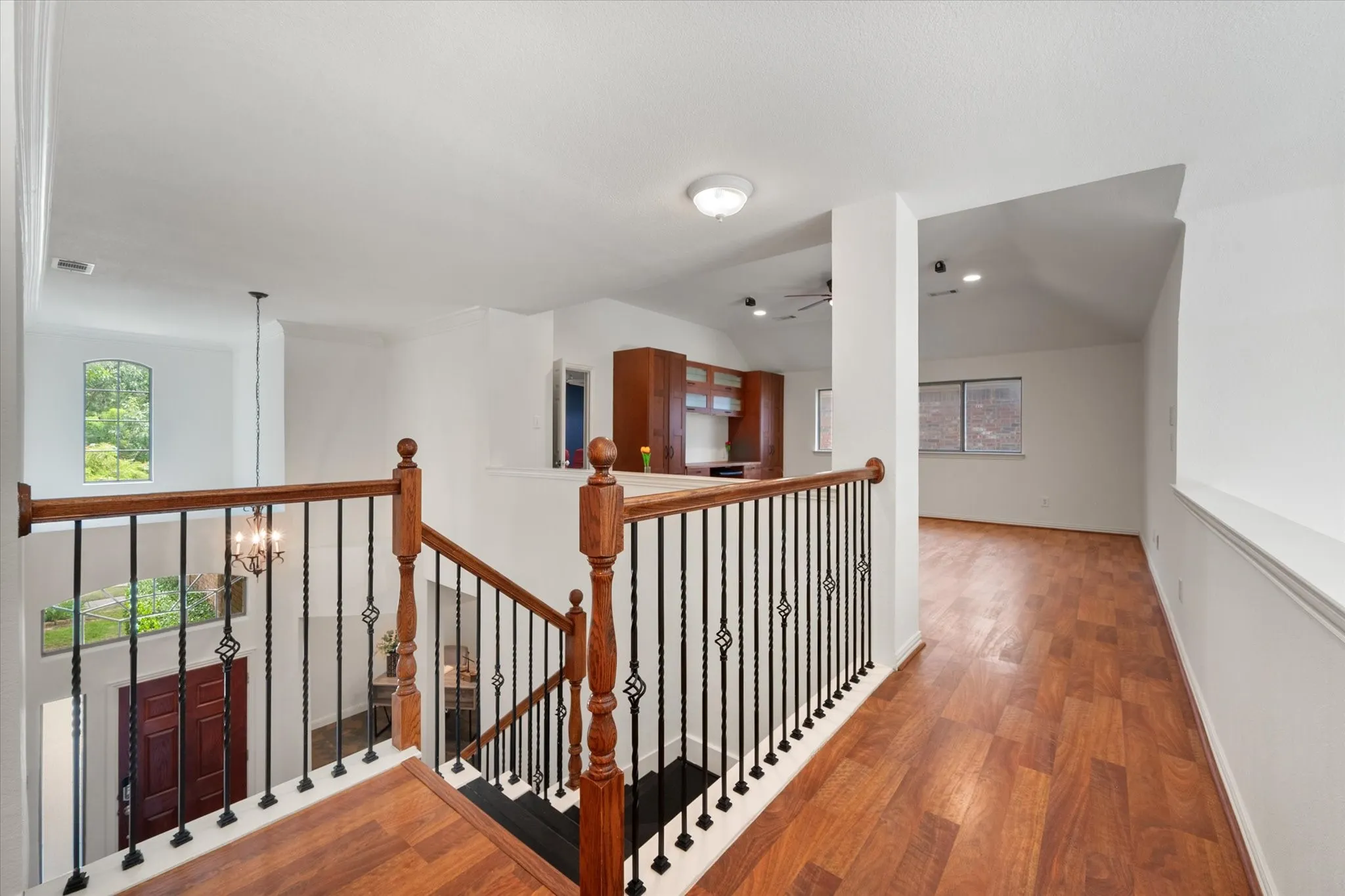 Upper-level landing with wood-finish flooring, white walls, and a wrought iron and wood baluster railing