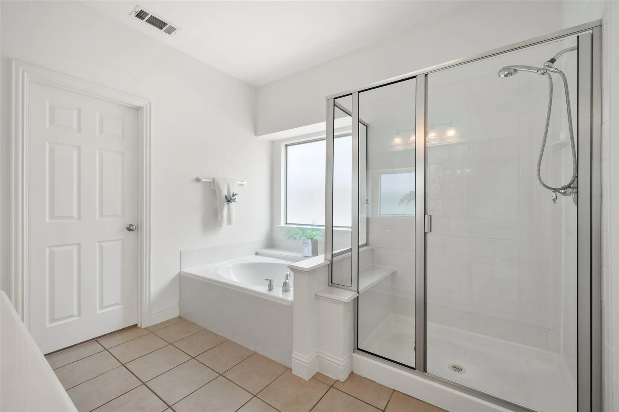 Bathroom featuring a built-in tub, separate glass-enclosed shower with a bench, frosted window, white panel door, and tile flooring