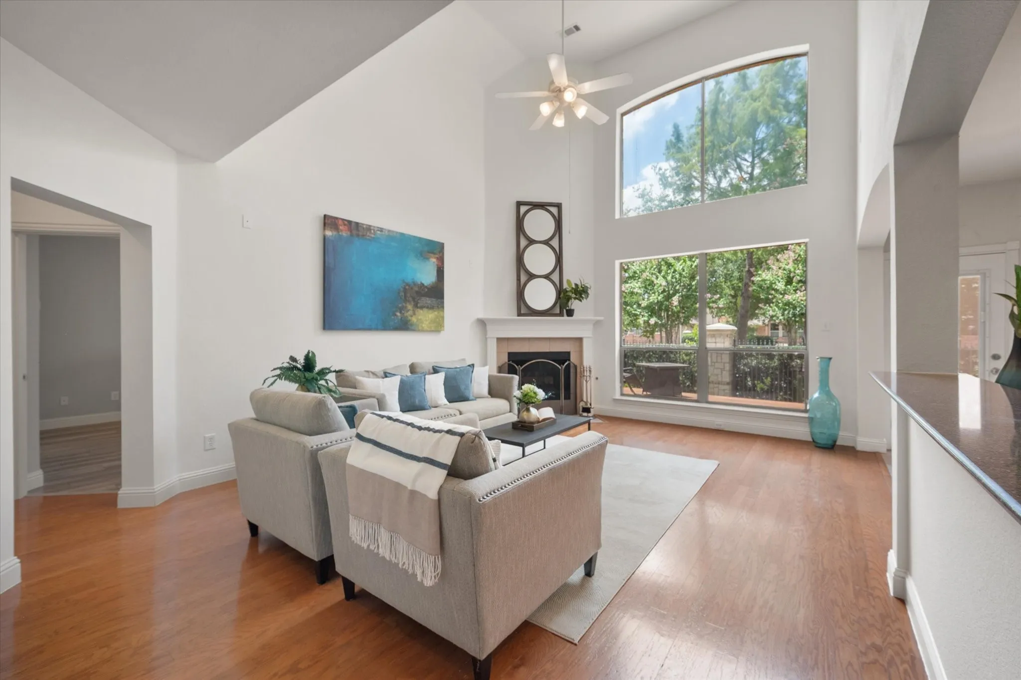 Living area featuring high vaulted ceilings, expansive windows, a fireplace with a mantel, a ceiling fan, and wood-finish flooring