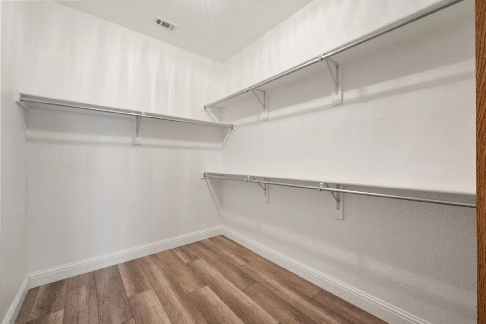 Primary Bedroom walk-in closet featuring wood-finish flooring, white baseboards, and multiple tiers of shelving with integrated hanging rods
