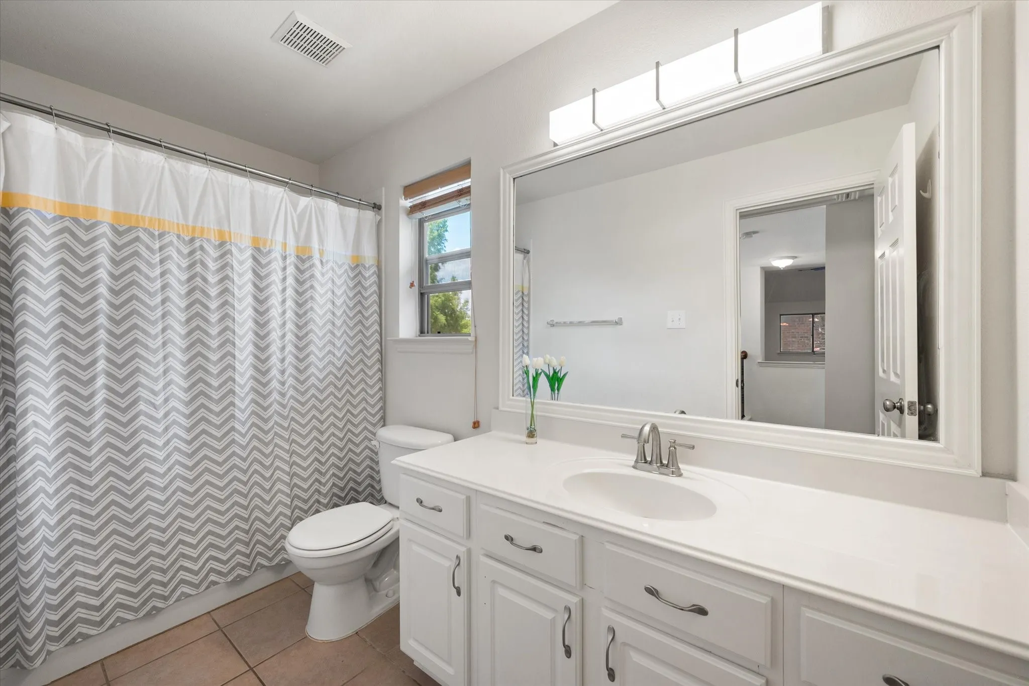Upstairs bathroom with white vanity with integrated sink, brushed nickel faucet, and a large framed mirror with overhead lighting