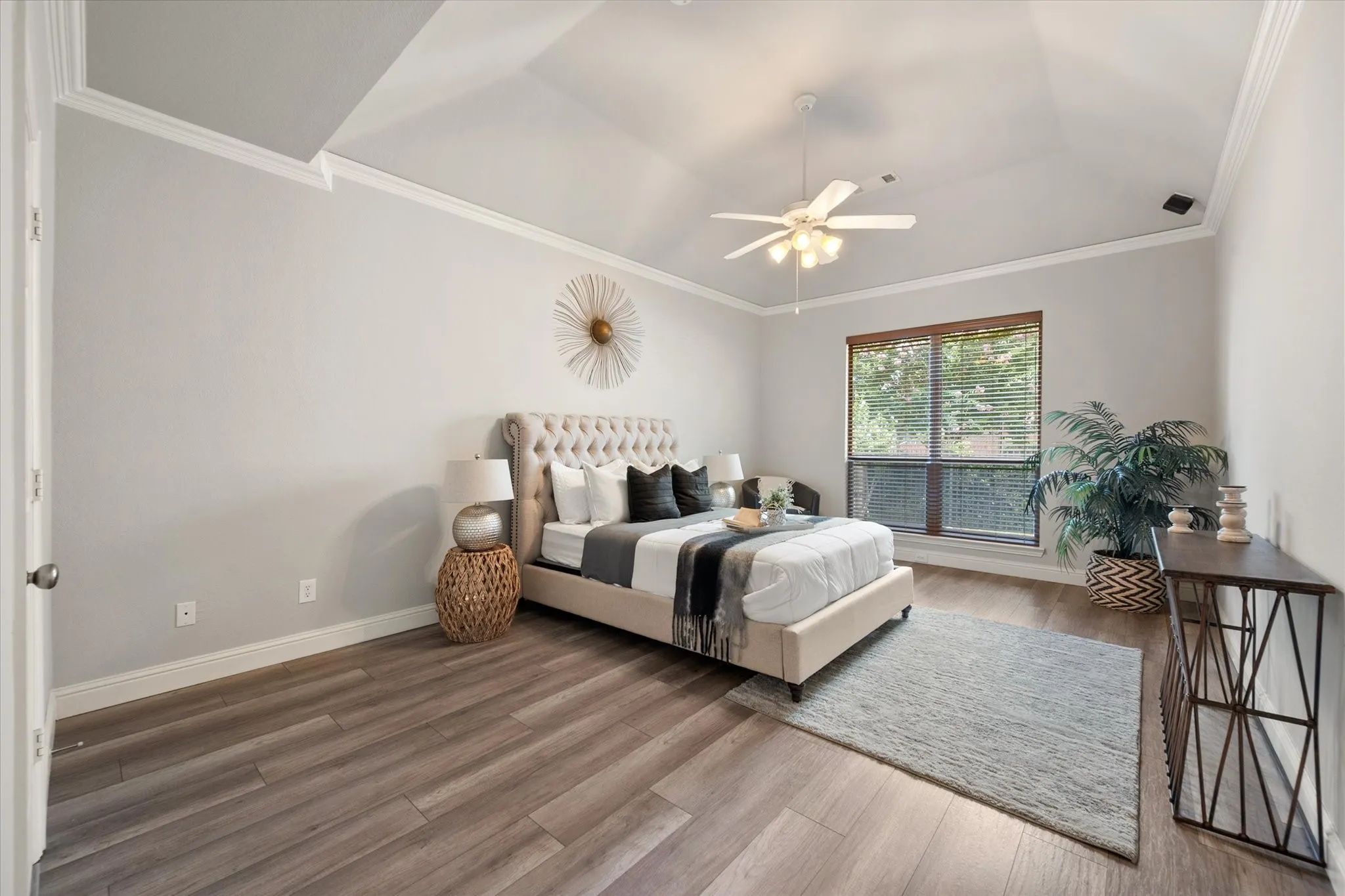 Spacious room featuring vaulted ceilings, wood-finish flooring, a large window with blinds, and crown molding